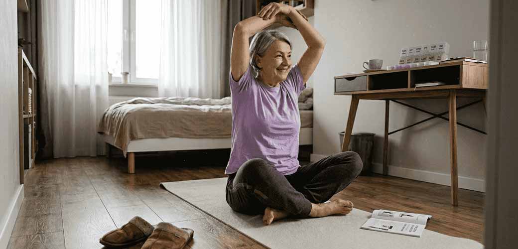 Starsza kobieta rozciąga ręce, ćwicząc na macie do jogi.